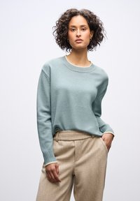 Miętowy sweter z okrągłym dekoltem i teksturowanymi rękawami, zestawiony z beżowymi spodniami o teksturowanej fakturze. Prosty design, miękka tkanina.