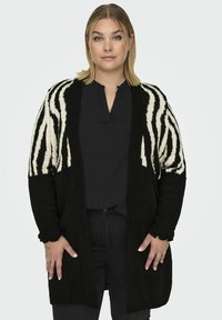 Zwart-wit gebreide cardigan met een zebra-streep patroon op de mouwen, een losse pasvorm en geribbelde manchetten.