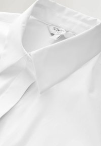 Cămașă albă din bumbac cu guler clasic, textură netedă și fără modele vizibile. Detaliu subtil de cusătură la guler. Etichetată "Next".