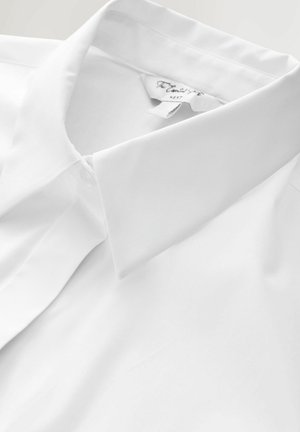 Biała bawełniana koszula z klasycznym kołnierzykiem, gładką fakturą i bez widocznych wzorów. Subtelne przeszycia przy kołnierzyku. Metka z napisem „Next”.