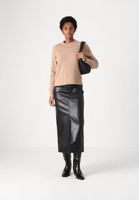 Beiger gerippter Pullover, schwarze Leder-Midi-Rock mit Schlitz vorne, schwarze kniehohe lacklederne Stiefel und eine geflochtene schwarze Handtasche.