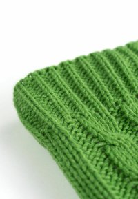 Grüner Strickstoff mit geripptem Muster, der eine glatte, weiche Oberfläche und dezente Zopfmuster-Details aufweist, schräg dargestellt.