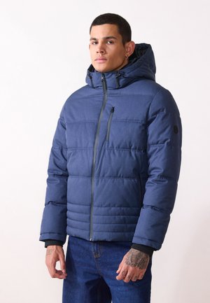 Chaqueta acolchada azul con capucha, que presenta un acolchado horizontal, cierre frontal con cremallera y un pequeño bolsillo en el pecho. Fabricada con un tejido de textura suave.
