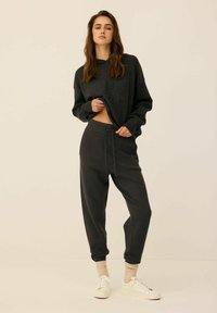 Ciemnoszara bluza z tłoczonym logo "UNIVERSE ATHLETICS", w zestawie z dopasowanymi, zwężającymi się spodniami dresowymi i białymi sneakersami.