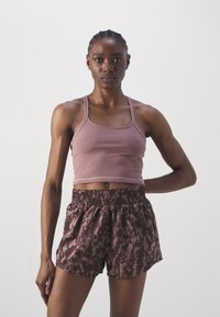 Licht mauve sportbeha met dunne bandjes, gedragen met bruin gestreepte shorts met een elastische tailleband en een losse pasvorm.