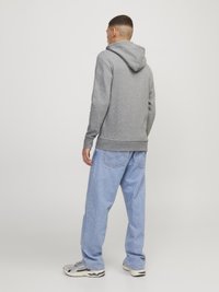 Sweat-shirt à capuche gris au style décontracté, associé à un jean en denim bleu clair. Le tissu semble doux et texturé. Des baskets grises et noires.