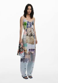 Maxikleid mit buntem Patchwork-Design, das florale, geometrische und vintage Muster zeigt. Spaghettiträger, transparenter Stoff und geschichtete Elemente.