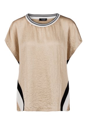 Blouse beige à manches courtes avec texture froissée, panneaux latéraux diagonaux noirs et blancs, et encolure blanche avec rayures noires.