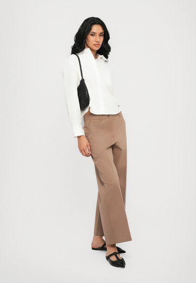 Chemise blanche à boutons, pantalon large marron, sac à main noir en tressé, et chaussures plates noires. Tissu lisse et couleurs neutres, design simple.
