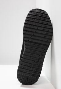 Black rubber shoe sole featuring textured surface with grooves and patterns for grip, tapering towards the edges with a smooth finish.