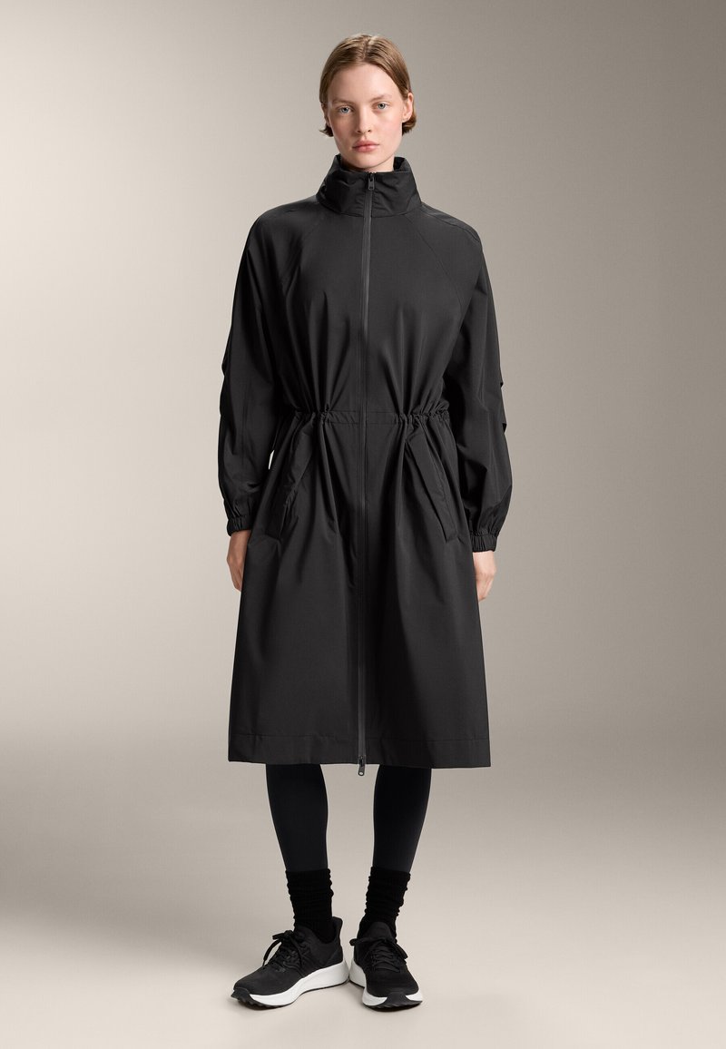 Zwarte waterafstotende jas met lange mouwen, hoge ritse kraag, getailleerde taille, zijzakken en verstelbare mouwen. Glad stoffen afwerking.