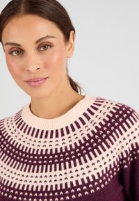 Maglione lavorato a maglia con scollatura rotonda rosa, caratterizzato da un motivo geometrico viola e rosa che attraversa il petto e le spalle. Morbida texture.