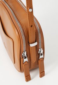 Borsa in pelle marrone chiaro con doppie cerniere argentate, forma strutturata e tracolla removibile con dettagli di cucitura. Texture liscia con una tasca frontale.