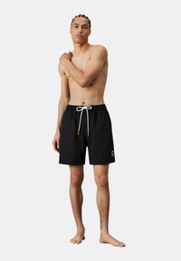Pantaloni da nuoto neri con vita regolabile, lacci bianchi e punte arancioni. Presenta un piccolo logo sul lato sinistro anteriore. Texture liscia.