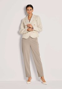 Beige tweed blazer met rafelige randen en gouden knopen, gecombineerd met beige op maat gemaakte broeken en crèmekleurige puntige hakken. Zilveren oorringen.