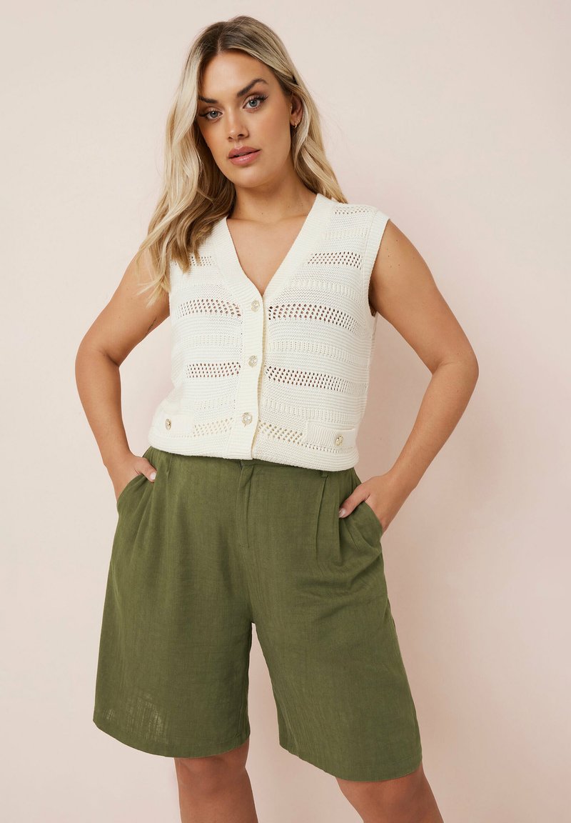 Vit stickad väst med V-ringning och knäppning, kombinerad med lösa olivgröna shorts med sidofickor och en texturerad tyg.