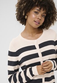 Striped cardigan in soft fabric, featuring alternating cream and dark navy stripes, round neckline, and button closure.