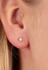 Silberner Ohrstecker mit einem klaren, facettierten Zirkonia-Stein, der in einer schlichten, runden Metallbasis gefasst ist, Nahaufnahme am Ohr.