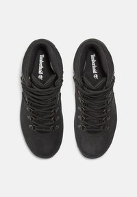 Stivali da escursionismo neri con un esterno in pelle liscia, alto supporto della caviglia, occhielli in metallo e spesse lacci neri. Marchio Timberland visibile all'interno.