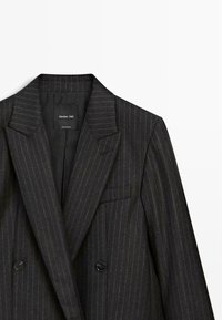 Blazer grigio scuro con righe sottili, colletto a fascia, frontale doppiopetto e due bottoni. Etichetta visibile sul collo. Design strutturato.