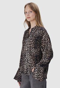 Luipaardprint blouse met een kraag, lange mouwen en een losse pasvorm, met een zwarte achtergrond en tan vlekken, gemaakt van een zachte stof.