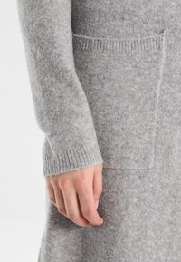 Ljust grått ullplagg med ribbad mudd och en framficka, med en mjuk textur och en lös passform.