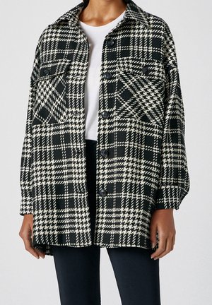Veste oversize à carreaux noir et blanc avec fermeture à boutons, deux poches poitrine, un col et une coupe décontractée. Le tissu présente une finition texturée.