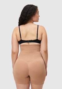 Beżowe szorty modelujące o gładkiej fakturze, długości do połowy uda, z regulowanymi czarnymi paskami. Charakteryzują się bezszwowym designem dla komfortu.