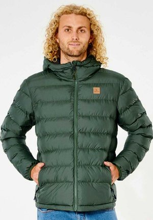Chaqueta acolchada verde con cremallera frontal, puños elásticos y capucha. Presenta un parche de logo en color beige en el pecho y un diseño acolchado.