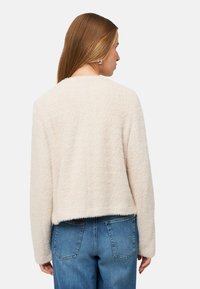 Kremowy, teksturowany, puszysty kardigan z zaokrąglonym dekoltem, krótkim krojem i długimi rękawami, zestawiony z wysokim stanem niebieskich jeansów.