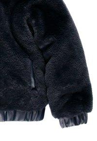 Czarna kurtka z futra ekologicznego o puszystej teksturze, z elastycznymi mankietami i skórzanym wykończeniem na dole. Brak widocznych zapięć lub wzorów.