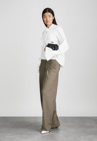 Blusa bianca con maniche a volant, colletto alto; pantaloni larghi a quadri marroni; tiene una pochette nera con chiusura metallica; tacchi bianchi a punta.