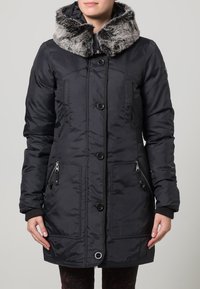 Svart vadderad jacka med fuskpälskrage, försedd med dragkedja fram, knäppning med knappar och två sidofickor med dragkedjedetaljer.