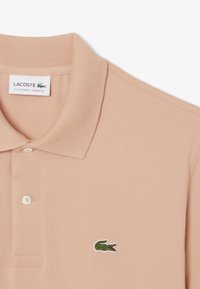 Pikétröja i ljus persika, med en klassisk passform. Har ett texturerat bomullsmaterial och en grön broderad krokodil-logga på bröstet.