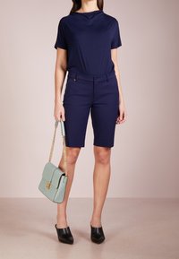 Haut à manches courtes bleu marine, short bleu marine ajusté, mules noires et sac à main vert clair avec une bandoulière en chaîne. Tissu lisse et design structuré.