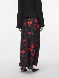 Long navy skirt with red rose print, made of smooth fabric. Worn with a black fitted jacket and paired with black heeled shoes.
