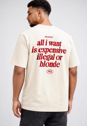 Mann mit kurzen lockigen Haaren und Bart trägt ein cremefarbenes T-Shirt mit rotem Text auf dem Rücken mit der Aufschrift "all i want is expensive illegal or blonde."