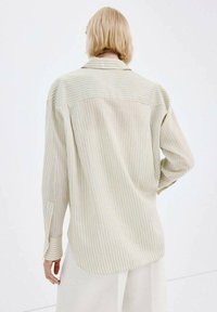 Koszula z długim rękawem w jasnobeżowym materiale z subtelnymi niebieskimi paskami, z kołnierzykiem na guziki i luźnym krojem.