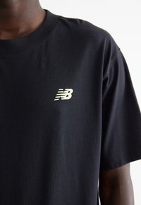 Camiseta de algodón negra con un pequeño logo blanco "NB" en la parte izquierda del pecho, mangas cortas y cuello redondo.