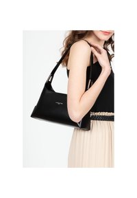 Sac à épaule en cuir noir avec une forme structurée, présentant une texture lisse et des accents métalliques sur les anses. Présenté sur un fond clair.