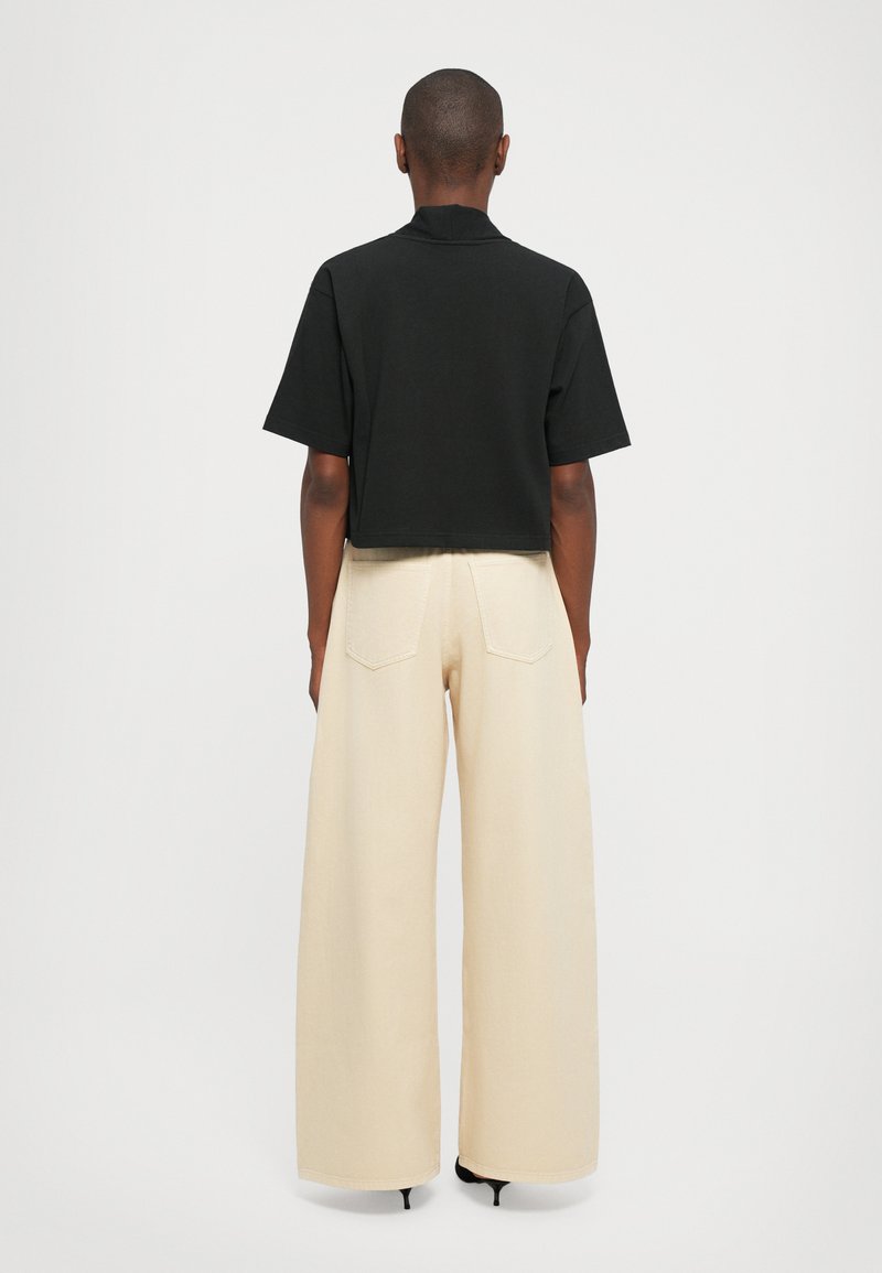Cropped black t-shirt with short sleeves, paired with wide-leg beige pants and black heels, viewed from the back.