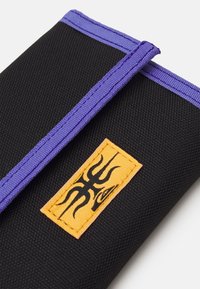 Black fabric wallet with purple trim, featuring a textured surface and an orange patch with a black design.