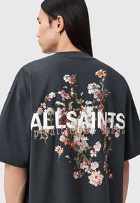 Μαύρο βαμβακερό μπλουζάκι με floral σχέδιο στην πλάτη. Το κείμενο γράφει «ALLSAINTS» με έντονα λευκά γράμματα, με ροζ και λευκά λουλούδια.
