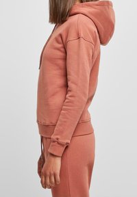 Sudadera color rosa con bolsillo frontal, capucha con cordón y puños acanalados. Tela suave y texturizada con un corte relajado.