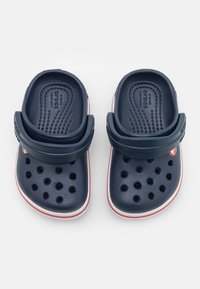 Sabots en plastique bleu avec plusieurs trous de ventilation, une bride arrière, des accents blancs et rouges, et une semelle texturée pour plus de confort.