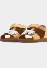 Παιδικά χρυσά σανδάλια με ανοιχτά δάχτυλα, ιμάντες με βέλκρο και λευκές διακοσμήσεις μαργαρίτας στους μπροστινούς ιμάντες.