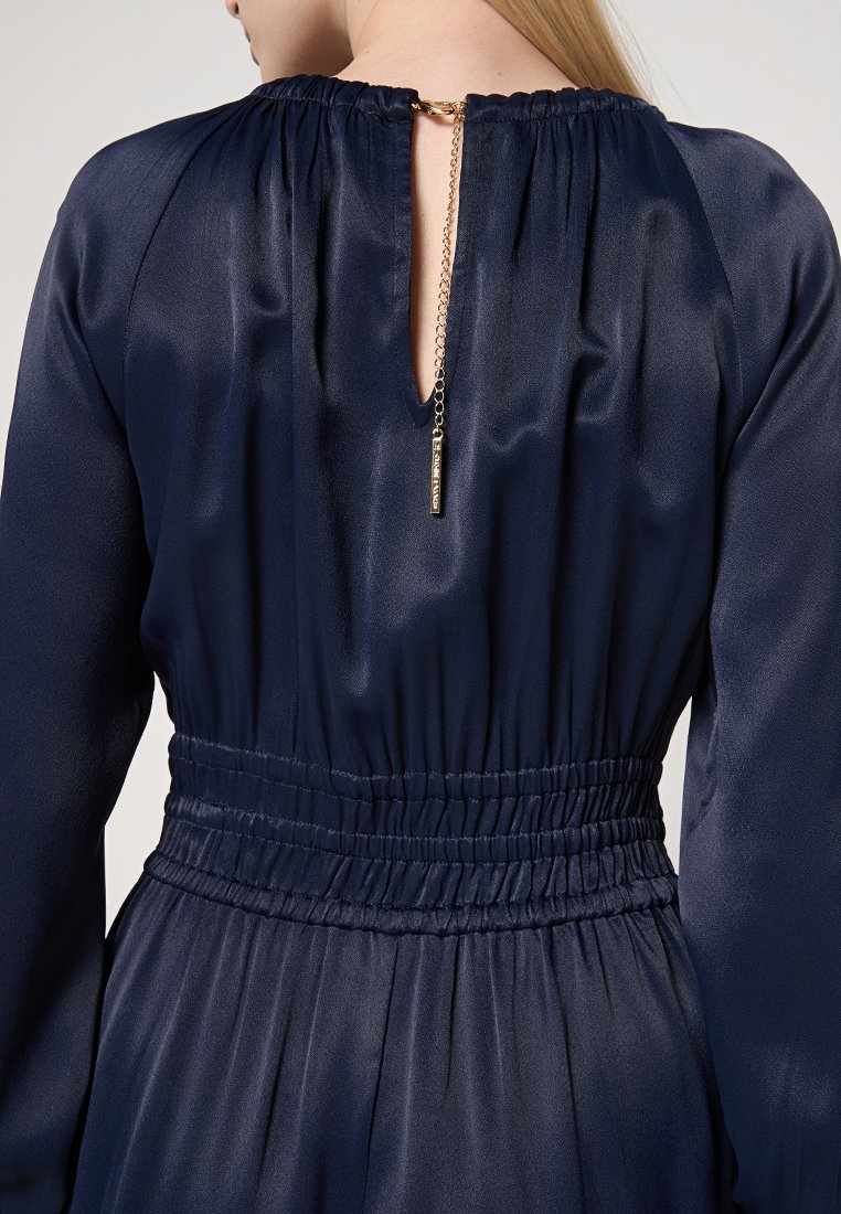 Abito di satin blu navy con vita elasticizzata, collo arricciato e schiena a chiave con dettaglio in catena dorata. Tessuto morbido e design fluido.
