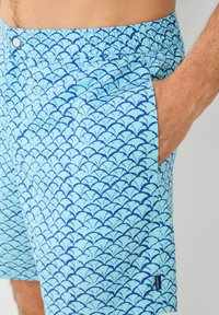 Plave kupalne kratke hlače s valovitim uzorkom u tamnoplavoj boji, izrađene od laganog materijala s elastičnim pojasom i bočnim džepovima.