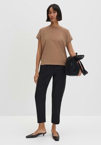 Maglietta a maniche corte a coste marrone abbinata a pantaloni neri su misura e mule nere con tacco. Modella che tiene una borsa di rete nera.