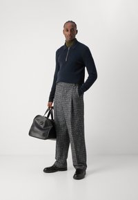 Pulover navy cu fermoar, pulover de culoare măslinie sub, pantaloni largi gri cu model tartan, geantă din piele neagră cu colțuri rotunjite, pantofi negri.